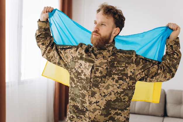 Foto porträt eines emotionalen jungen bärtigen ukrainischen patriotensoldaten in militäruniform, der eine flagge im büro hält