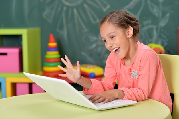 Porträt eines emotionalen kleinen Mädchens, das einen Laptop benutzt, während es am Schreibtisch im Klassenzimmer sitzt