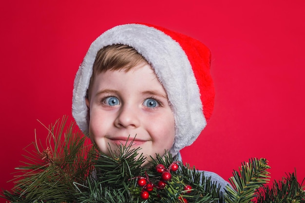 Porträt eines entzückenden kleinen Jungen, der eine Weihnachtsmütze auf rotem Grund trägt.