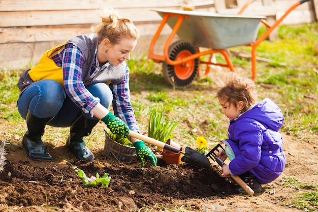 Porträt eines entzückenden Paares von Mutter und Tochter, die im Hinterhof ihres Landhauses arbeiten. Nettes Mädchen, das Mama hilft, Blumen zu pflanzen