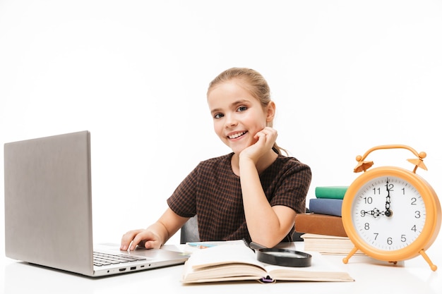 Porträt eines entzückenden Schulmädchens mit silbernem Laptop beim Lernen und Lesen von Büchern in der Klasse isoliert über weißer Wand