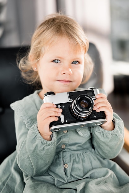 Porträt eines entzückenden, süßen Mädchens, das in den Armen eine kleine Fotokamera hält, die stilvoll trägt