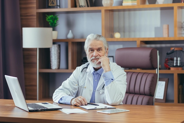 Porträt eines erfahrenen Arztes mit grauem Haar, der im Büro arbeitet und in die Kamera schaut