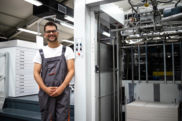 Foto porträt eines erfahrenen typographen, der in der druckerei an einer modernen druckmaschine steht.