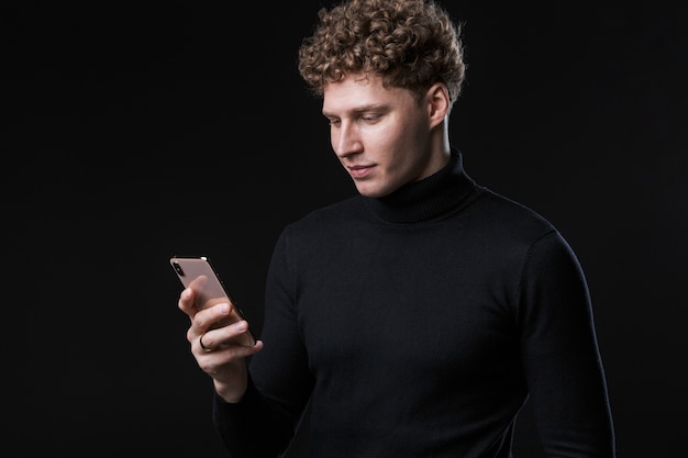 Porträt eines erfolgreichen, fröhlichen jungen, attraktiven, lockigen Geschäftsmannes, der vor einer schwarzen Wand steht und mit dem Handy spricht