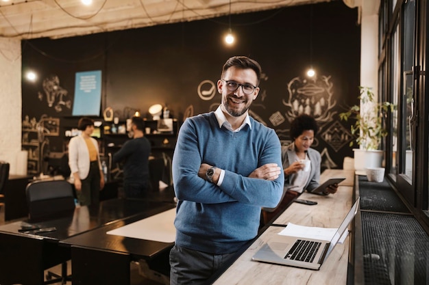 Porträt eines erfolgreichen Geschäftsmannes, der neben einem Laptop im Café steht