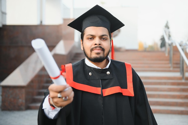 Porträt eines erfolgreichen indischen Studenten im Abschlusskleid mit dem Daumen nach oben