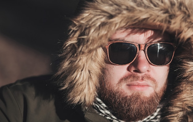 Porträt eines ernsten bärtigen Mannes, der Winter-Alaska-Jacke und -Sonnenbrille trägt