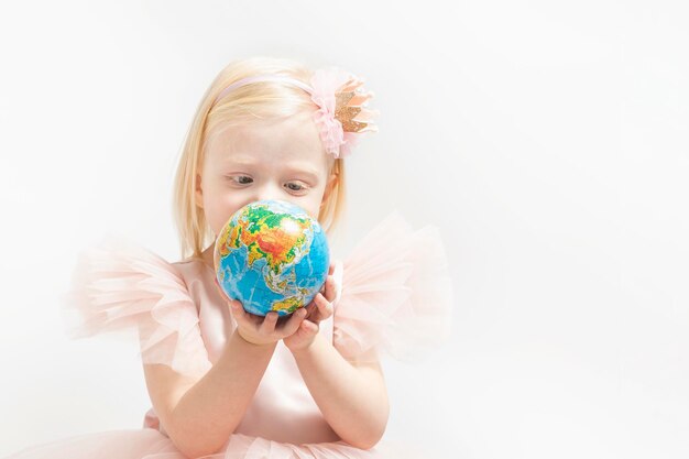 Porträt eines ernsthaften blonden kleinen Mädchens mit Globushänden Kind mit weißen Haaren trägt ein rosa Kleid mit Puffärmeln