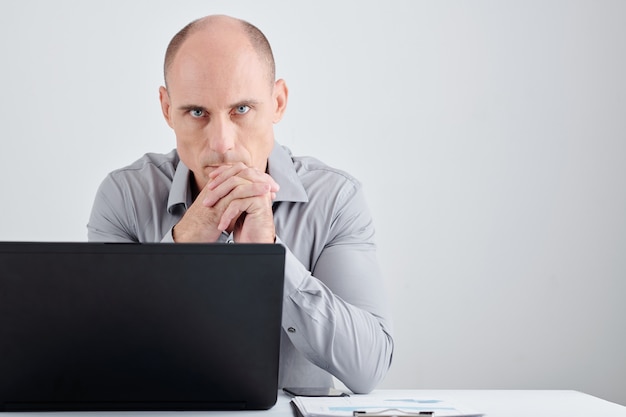 Foto porträt eines ernsthaften reifen unternehmers, der mit geöffnetem laptop am schreibtisch sitzt