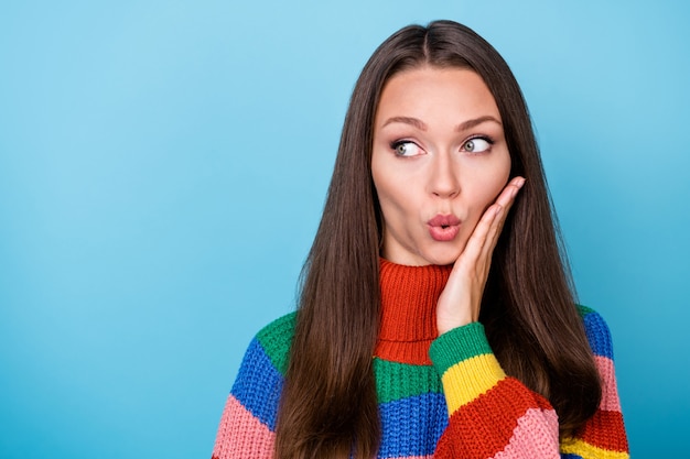 Porträt eines erstaunten Mädchens, das Kopienraum beeindruckt, Gerücht, Klatsch, geheime Berührung, Hand, Gesicht, Regenbogenpullover, isoliert auf blauem Hintergrund, tragen