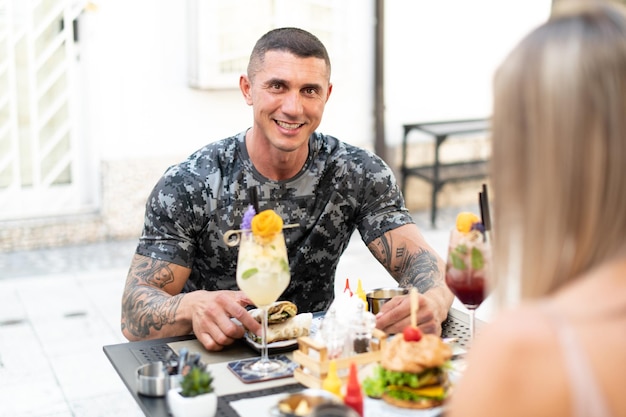 Porträt eines erwachsenen Mannes, der im Freien Tortilla oder Burrito im Restaurant isst und Cocktail trinkt