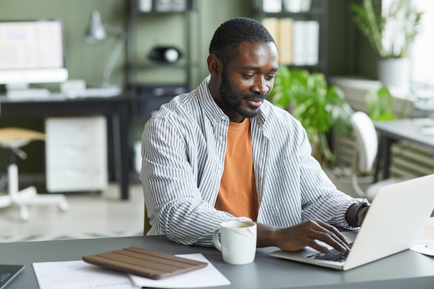 Porträt eines erwachsenen schwarzen Mannes, der zu Hause im Büro arbeitet und Laptop-Kopienplatz nutzt