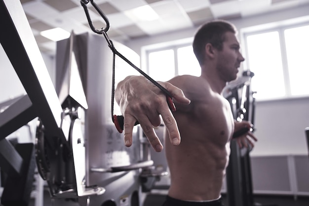 Porträt eines Fitnesssportlers mit muskulösem Körper macht Übungen an Sportgeräten im Fitnessstudio, trainiert Armmuskeln, pumpt Bizeps und Trizeps