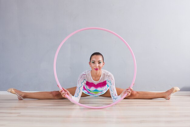 Porträt eines flexiblen Turnermädchens, das akrobatische Kunststücke mit rosa Hoop macht