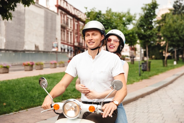 Porträt eines freudigen jungen Paares in den Helmen, die zusammen auf einem Motorrad auf der Stadtstraße fahren