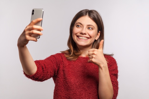 Porträt eines freundlichen Mädchens, das einen Videoanruf über das Handy macht und Daumen hoch zeigt, kommuniziert