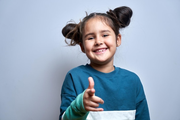 Porträt eines freundlichen, positiven jungen Mädchens wählt Ihr Kind, das mit dem Finger auf die Kamera zeigt, die auf weißem Hintergrund isoliert ist