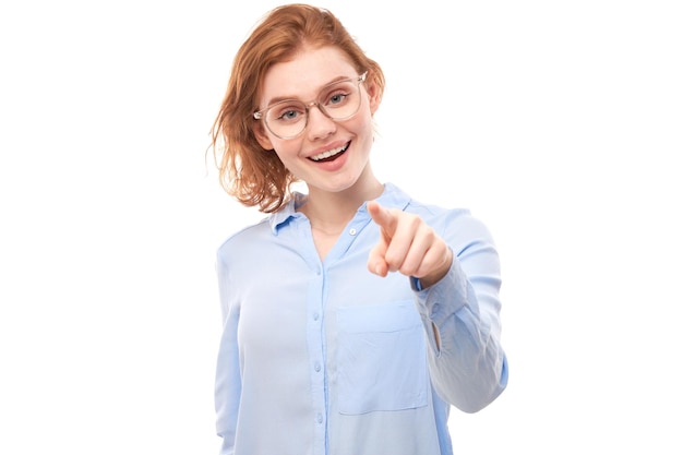 Porträt eines freundlichen rothaarigen Mädchens, das Sie mit dem Finger auf die Kamera zeigt, die auf weißem Hintergrund isoliert ist