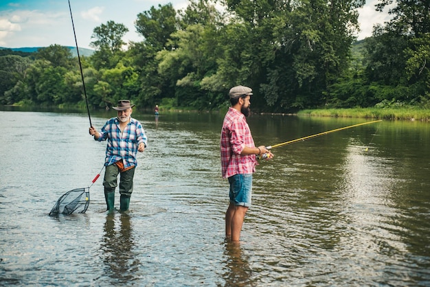 Porträt eines fröhlichen älteren Mannes, der Großvater und Sohn fischt, junger Mann und ein Fisch des alten Mannes