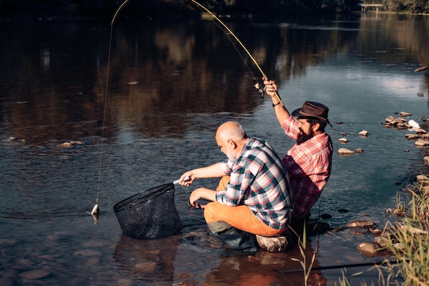 Porträt eines fröhlichen älteren Mannes, der Großvater und Sohn fischt, junger Mann und ein Fisch des alten Mannes