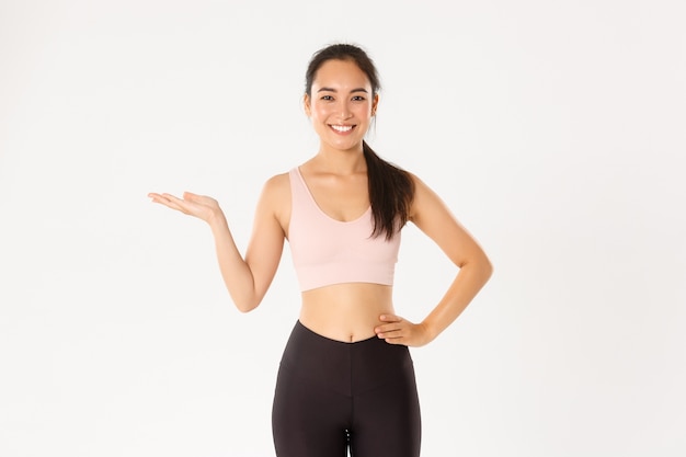 Porträt eines fröhlichen attraktiven asiatischen Fitnesstrainers, einer Sportlerin, die ein Produkt für das Training vorstellt oder demonstriert und etwas zur Hand hält.