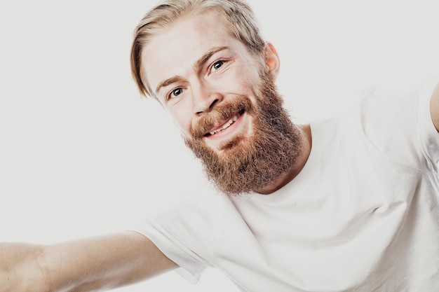 Porträt eines fröhlichen bärtigen Mannes, der ein Selfie auf weißem Hintergrund macht, hautnah