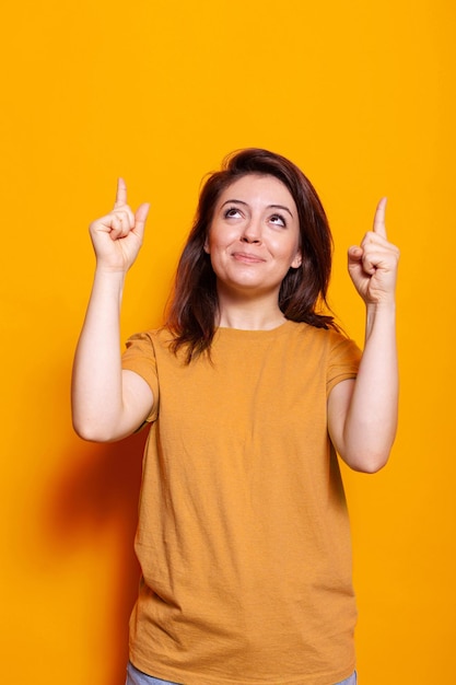 Porträt eines fröhlichen Erwachsenen, der mit dem Zeigefinger nach oben zeigt und lächelt. Fröhliche Person, die mit den Händen die Richtung zeigt und für die Fotografie im Studio nach oben zeigt. Werbe-Pose