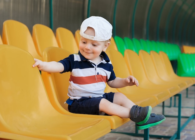 Porträt eines fröhlichen Jungen an einem Sommertag. Schönes Kind in einer Baseballmütze im Stadion in der Nähe der hellen Sitze.