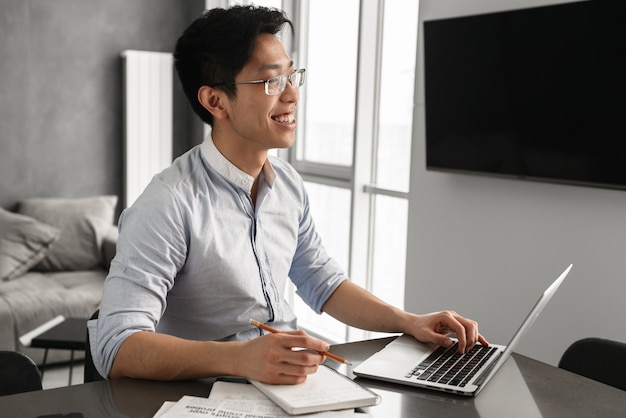 Porträt eines fröhlichen jungen asiatischen Mannes unter Verwendung des Laptops