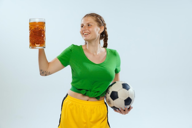Porträt eines fröhlichen jungen Mädchens mit Bierkrug, das die Fußballmannschaft unterstützt, die isoliert auf blauem Hintergrund posiert