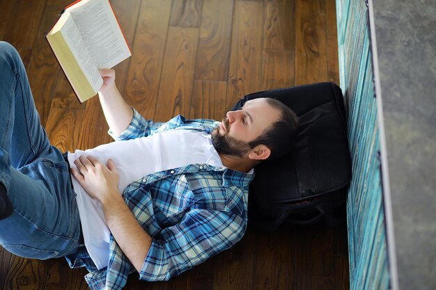 Porträt eines fröhlichen jungen Mannes, der ein Buch in seinem Wohnzimmer liestStudent, der ein Buch hält und liest