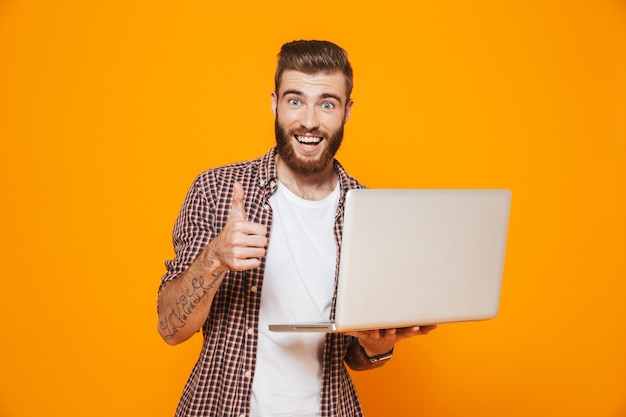 Porträt eines fröhlichen jungen Mannes, der Freizeitkleidung unter Verwendung des Laptops trägt