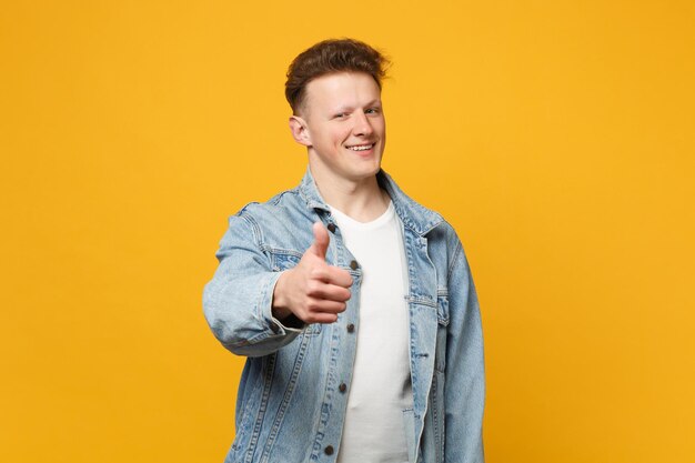 Porträt eines fröhlichen jungen Mannes in Denim-Freizeitkleidung, der die Kamera zeigt, die den Daumen isoliert auf gelb-orangefarbenem Wandhintergrund im Studio zeigt. Menschen aufrichtige Emotionen Lifestyle-Konzept. Mock-up-Kopienbereich.