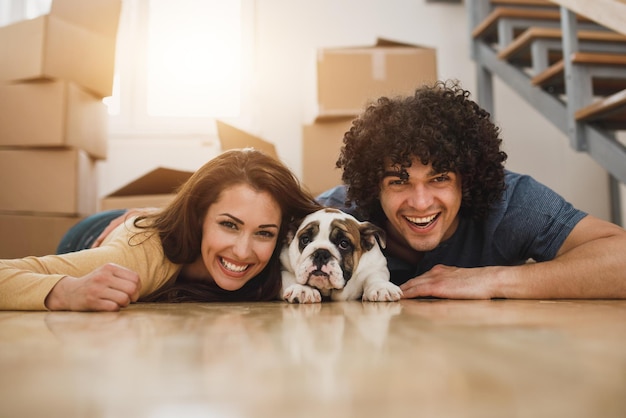 Porträt eines fröhlichen jungen Paares, das mit seinem englischen Bulldoggenwelpen posiert, während es in sein neues Zuhause einzieht. Blick in die Kamera.