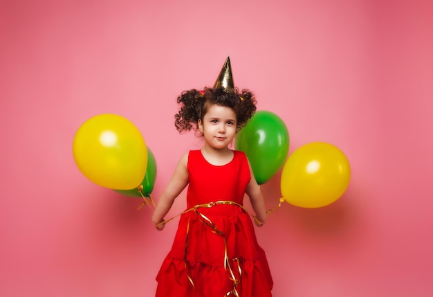 Porträt eines fröhlichen kleinen Mädchens isoliert auf einem rosa Hintergrund, das einen Haufen bunter Luftballons hält