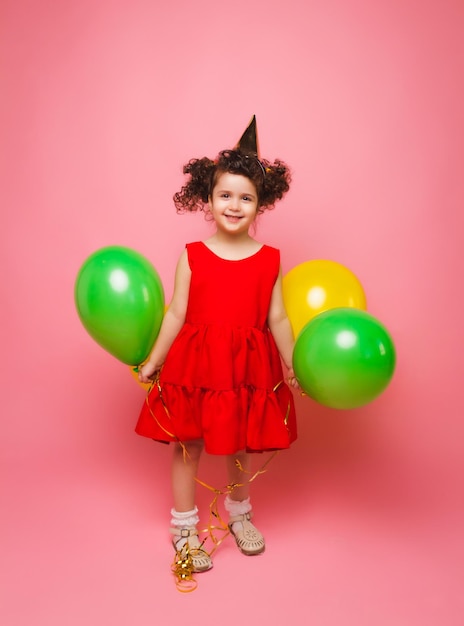 Porträt eines fröhlichen kleinen Mädchens isoliert auf einem rosa Hintergrund, das einen Haufen bunter Luftballons hält