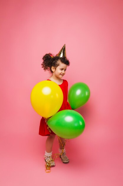 Porträt eines fröhlichen kleinen Mädchens isoliert auf einem rosa Hintergrund, das einen Haufen bunter Luftballons hält