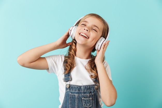Porträt eines fröhlichen kleinen Mädchens isoliert über blauer Wand, mit Kopfhörern