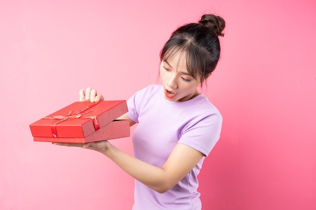 Porträt eines fröhlichen Mädchens, das in der Hand eine Geschenkbox öffnet, isoliert auf rosa Wand