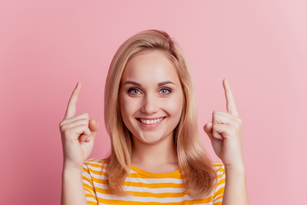 Porträt eines fröhlichen Mädchens zeigt Finger auf leeren Raum zahniges Lächeln auf rosa Hintergrund
