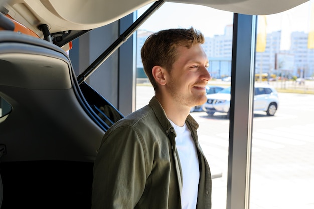 Porträt eines fröhlichen Mannes, der im Kofferraum seines neuen Autos sitzt Teure Anschaffung
