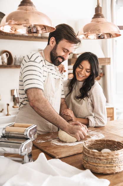 Porträt eines fröhlichen Paares, Mann und Frau der 30er Jahre, die Schürzen tragen, die den Teig mischen, während sie zu Hause zusammen in der Küche kochen