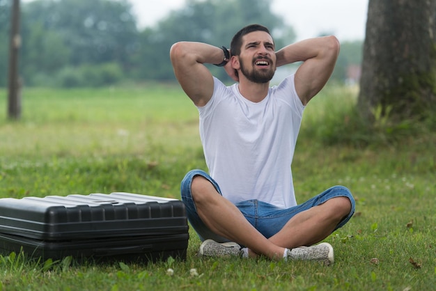 Porträt eines frustrierten jungen Ingenieurs, der mit einem Fall von einer Drohne auf Gras sitzt