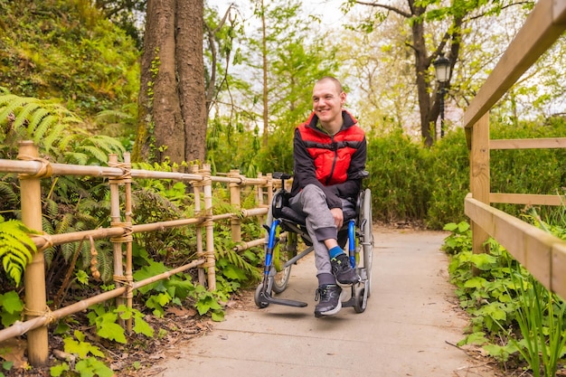 Porträt eines gelähmten jungen Mannes in einem öffentlichen Park in der Stadt, der im Rollstuhl sitzt und den Weg entlang schlendert