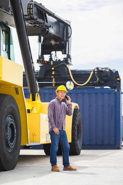 Porträt eines Geschäftsmannes am Telefon in Frachtcontainern, Vorarbeiteringenieur in Hardhat mit Smartphone in der Arbeitsjob-Import-Export-Geschäfts-kundenspezifischen logistischen Frachtterminal-Containerindustrie