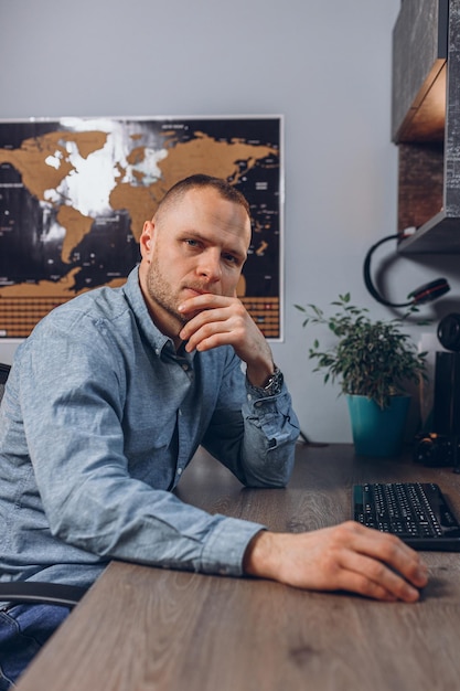 Porträt eines Geschäftsmannes, der aus der Ferne am Tisch mit einer Computermaus arbeitet und in die Kamera schaut