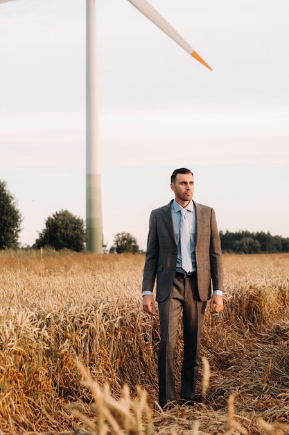 Porträt eines Geschäftsmannes in einem grauen Anzug auf einem Weizenfeld vor dem Hintergrund einer Windmühle und des Abendhimmels