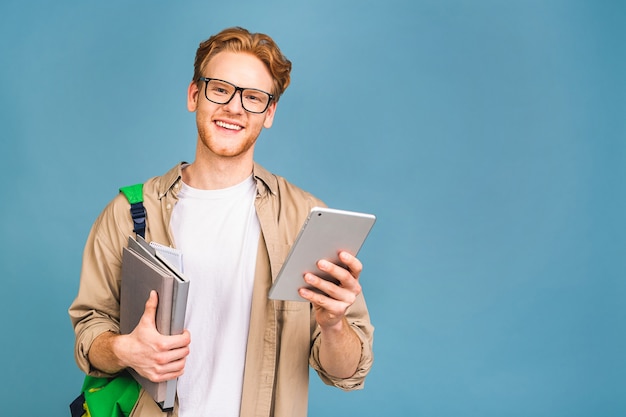 Porträt eines glücklich lächelnden jungen Studenten, der mit Rucksack und Ordnern steht. Tablet verwenden