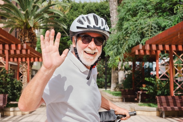 Porträt eines glücklichen älteren Radfahrers mit Helm, der mit einem Elektrofahrrad im öffentlichen Park der Stadt läuft und in die Kamera schaut Konzept eines gesunden Lebensstils und nachhaltiger Mobilität